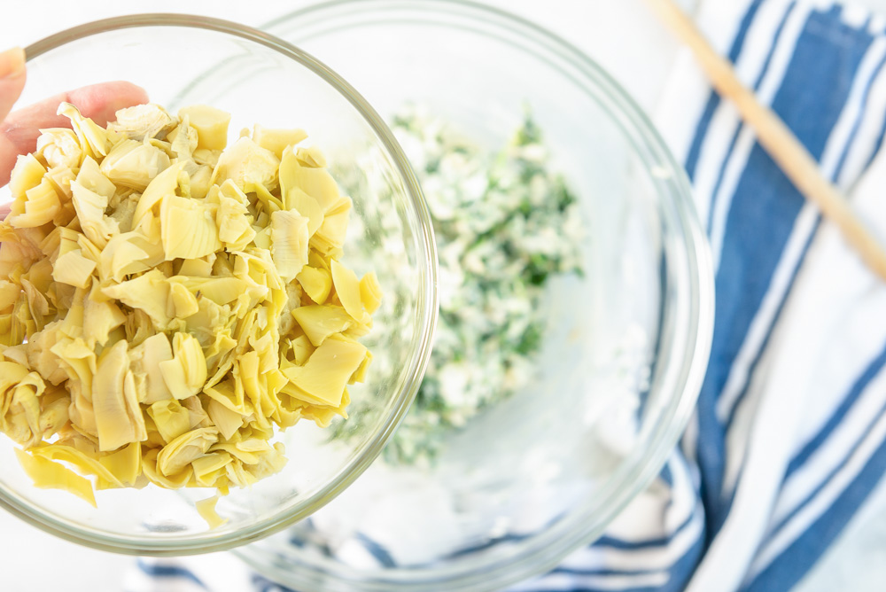 Artichoke hearts being added to artichoke dip