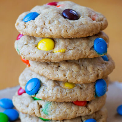 A stack of golden brown monster peanut butter cookies with colorful M&Ms on top.