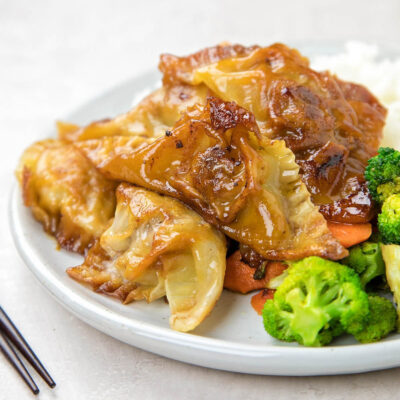 Homemade potstickers with steamed vegetables and rice on a white plate.