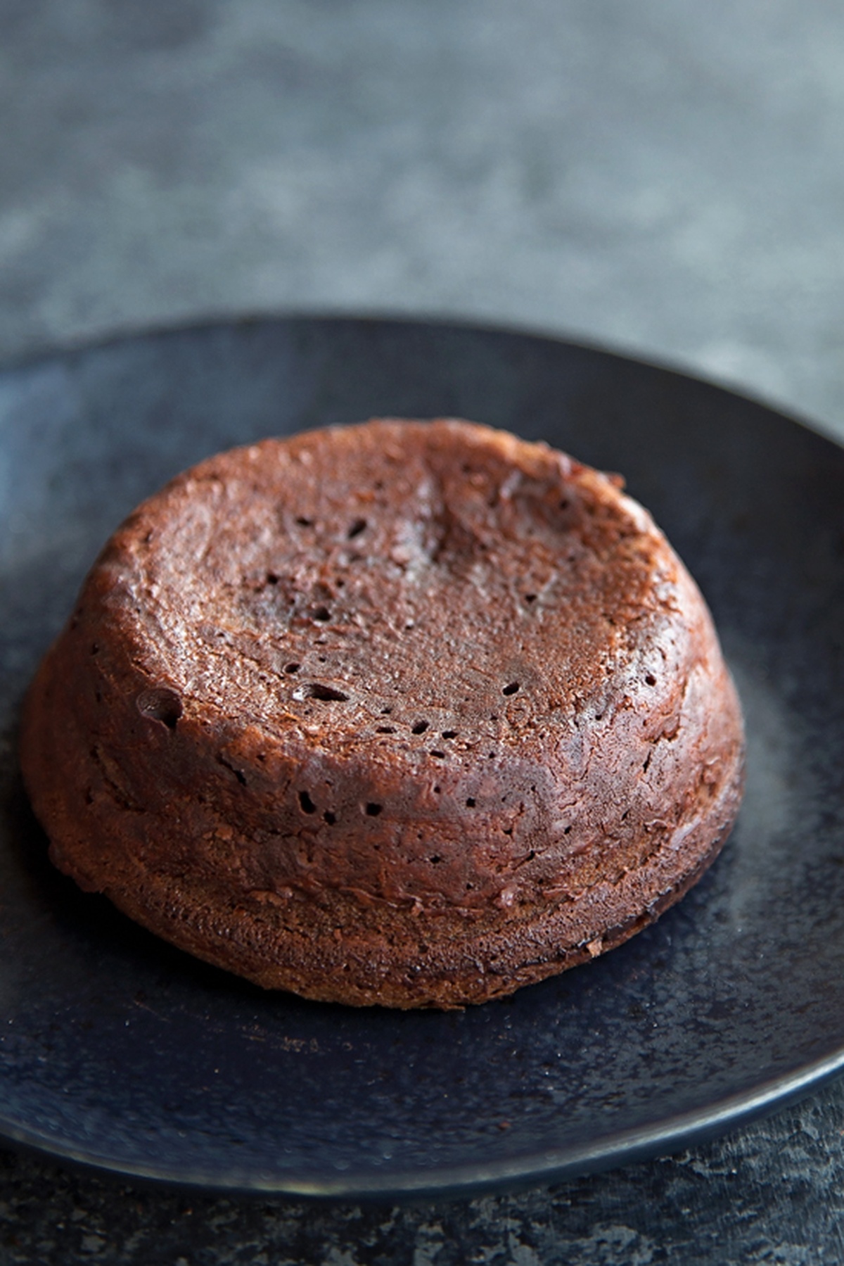 A plain, freshly baked chocolate molten lava cake served on a dark plate.