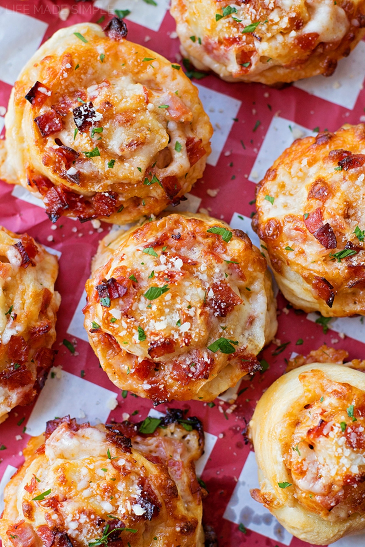 Golden-brown Pepperoni Pizza Pinwheels arranged on red and white parchment paper.