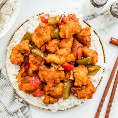 Homemade sweet and sour chicken served over white rice with chopsticks on the side.