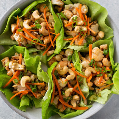 A plate of chicken and cashew lettuce wraps topped with shredded carrots and green onions.