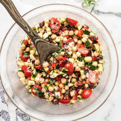 Zucchini chickpea salad being tossed with fresh herbs and dressing for even coating.