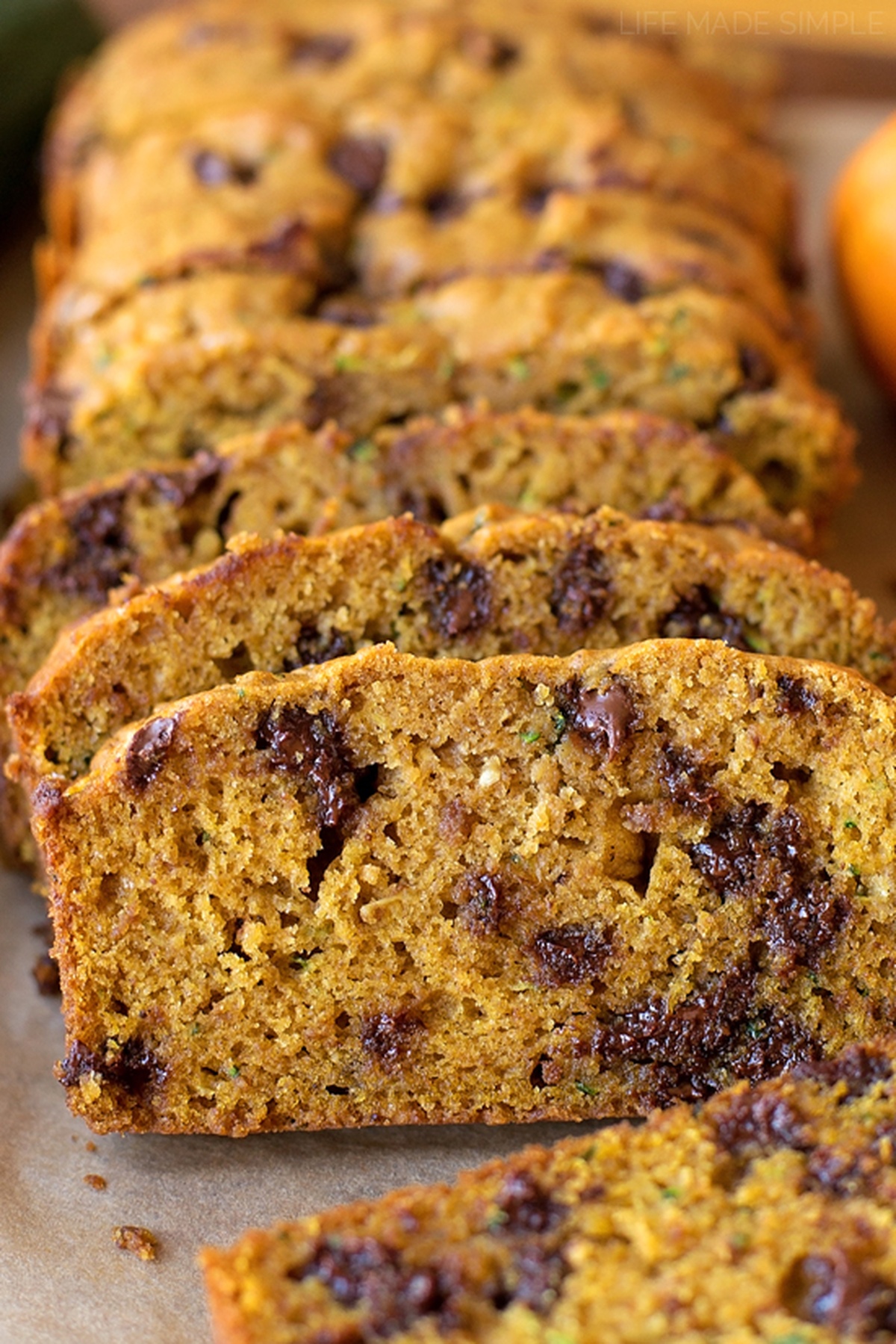 Pumpkin and spice adds a hint of fall to this moist and tender pumpkin zucchini bread. It's easy to make and even easier to customize! Slices of pumpkin zucchini bread with chocolate chips, arranged on parchment paper.