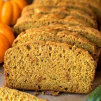Slices of pumpkin zucchini bread served on a white plate with crumbs scattered around.