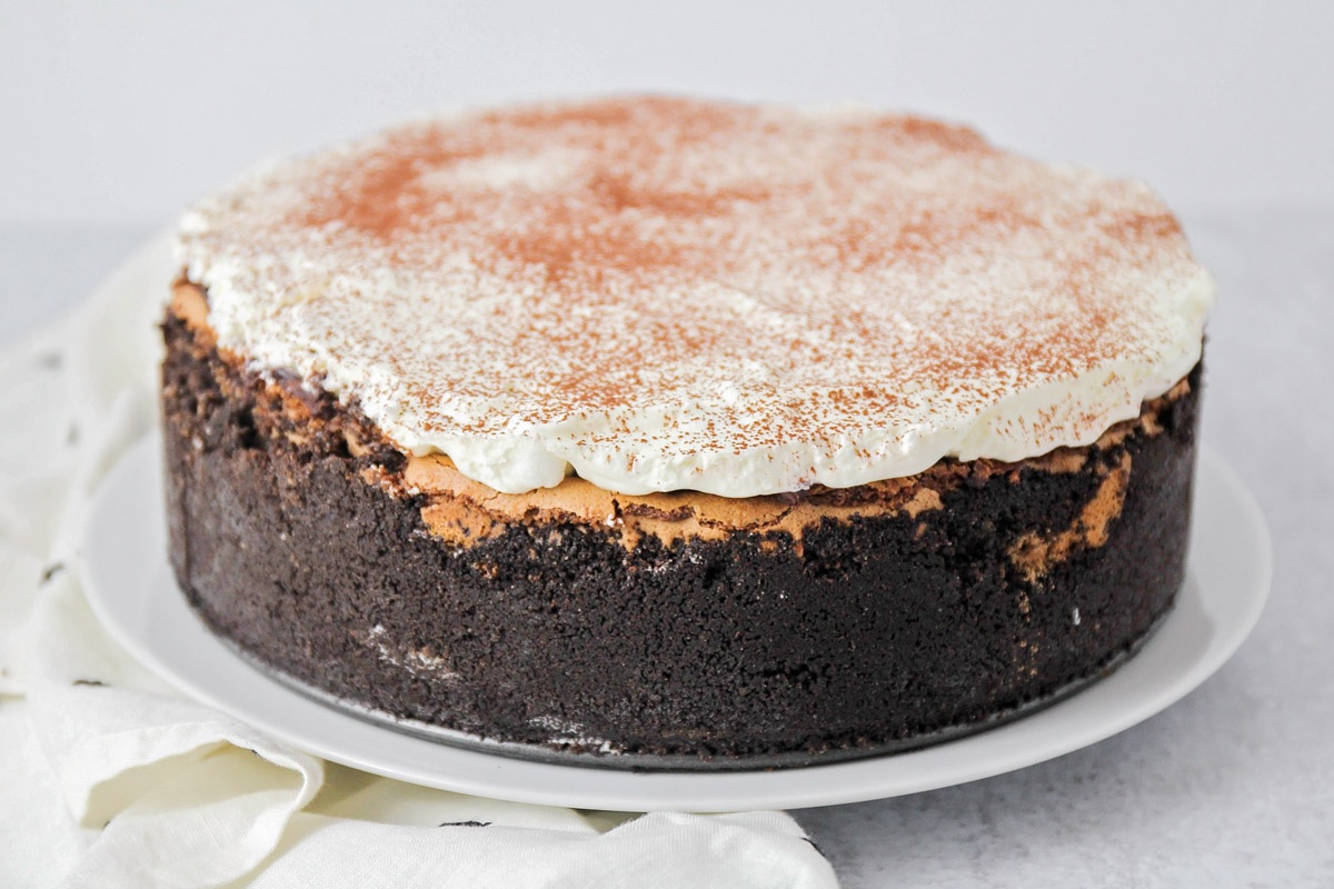 Fully assembled Mississippi Mud Pie with whipped cream spread over the marshmallow layer and dusted with cocoa powder.