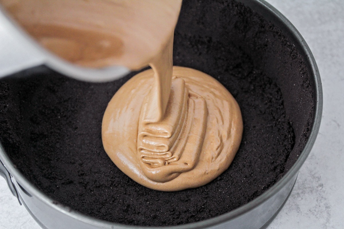Chocolate batter being poured into the prepared crust in the springform pan.