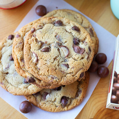 A stack of freshly baked Whopper cookies on parchment paper surrounded by Whoppers candy.