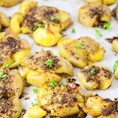 Smashed potatoes roasted in the oven on a parchment-lined baking sheet.
