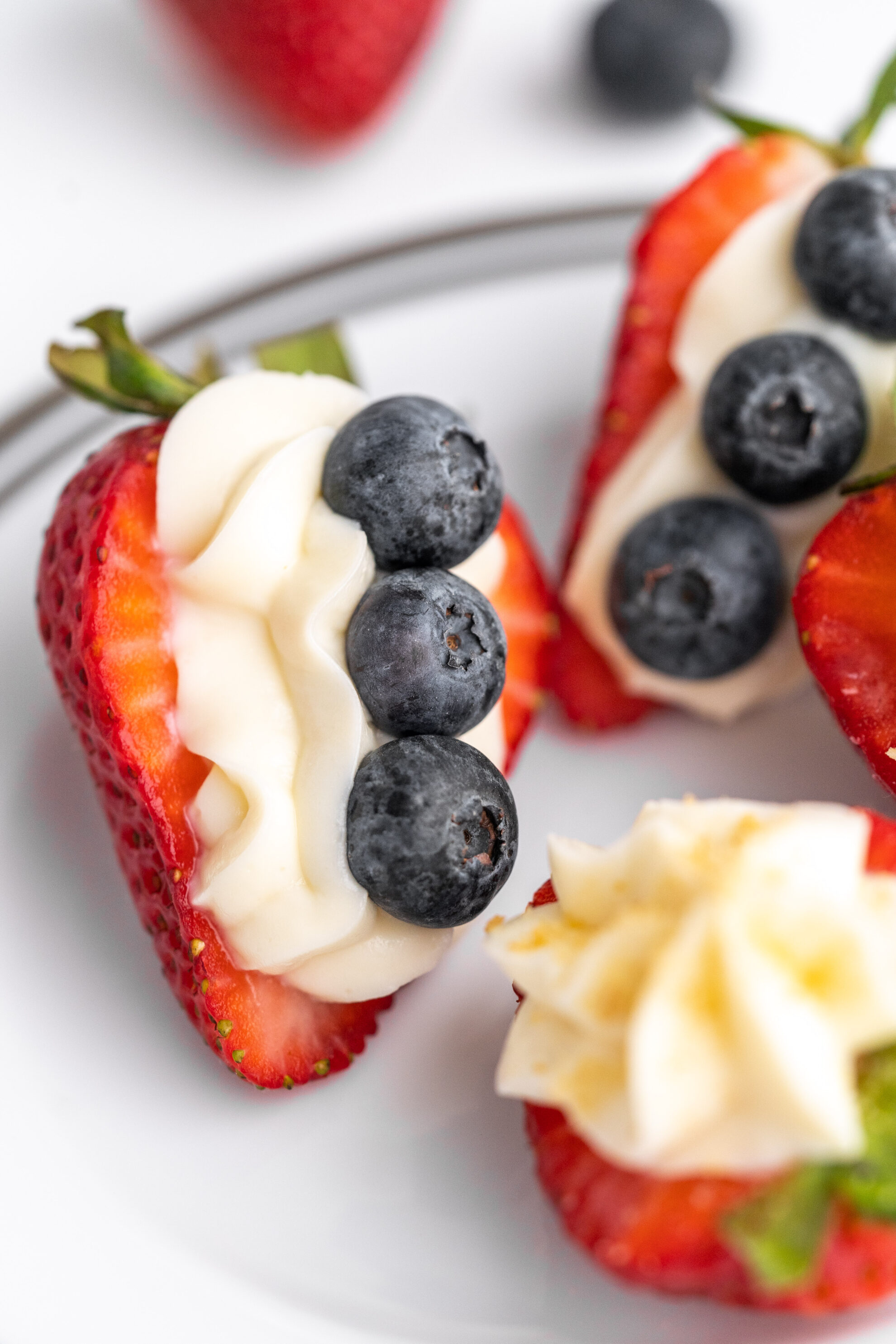 cream stuffed strawberries recipe with blueberries sitting on a white plate