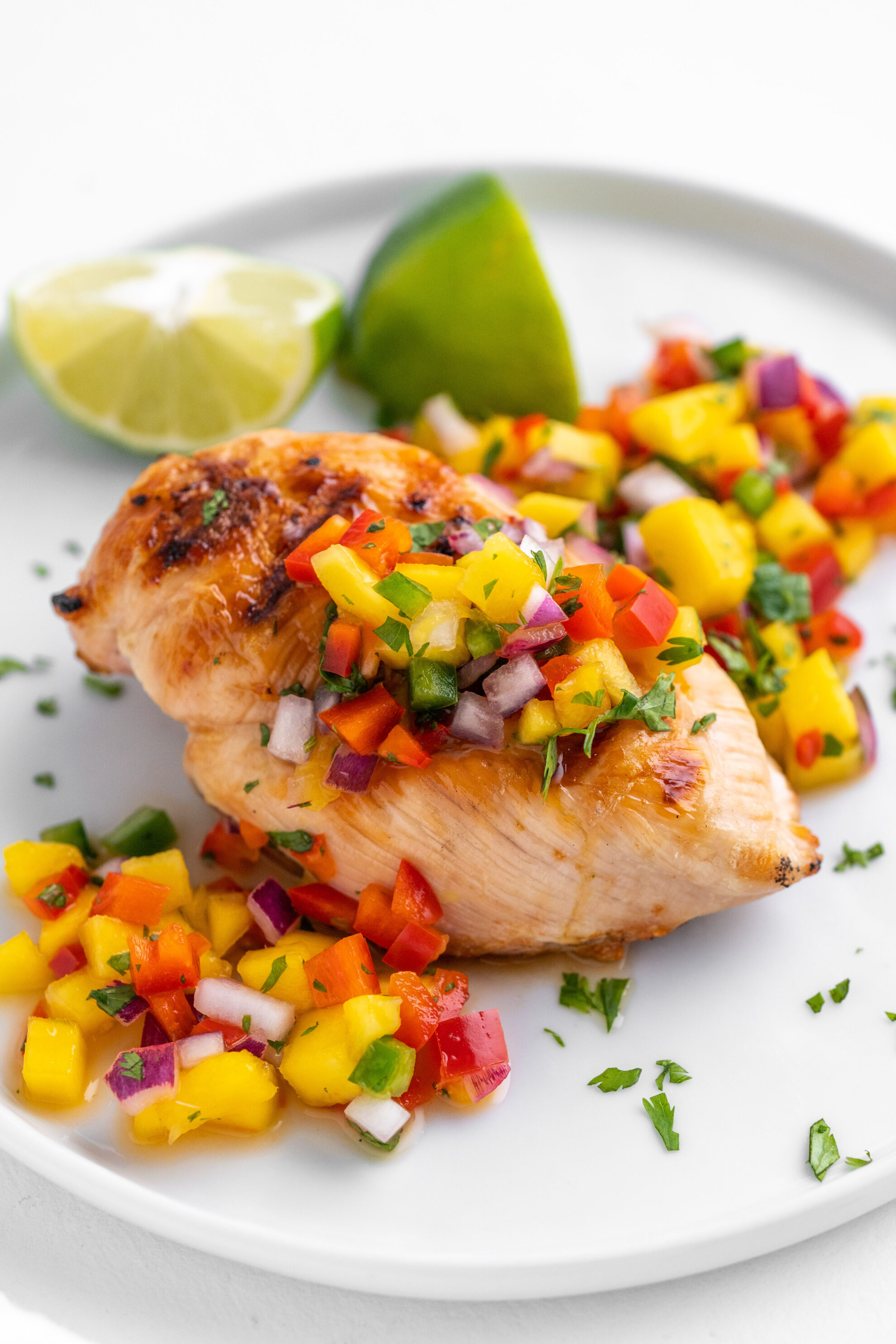 mango pico recipe on top of a grilled chicken breast on a white plate
