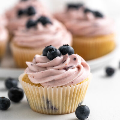 Blueberry cupcake on a flat surface with scattered blueberries around it.
