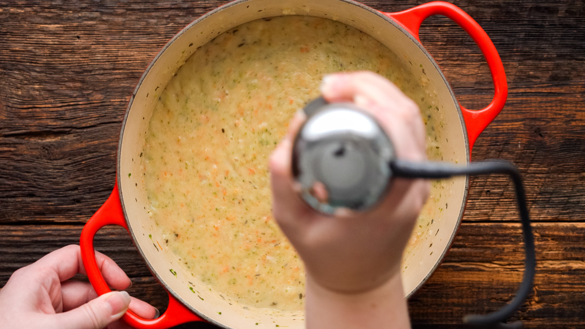 Blending the soup to the perfect consistency using an immersion blender.