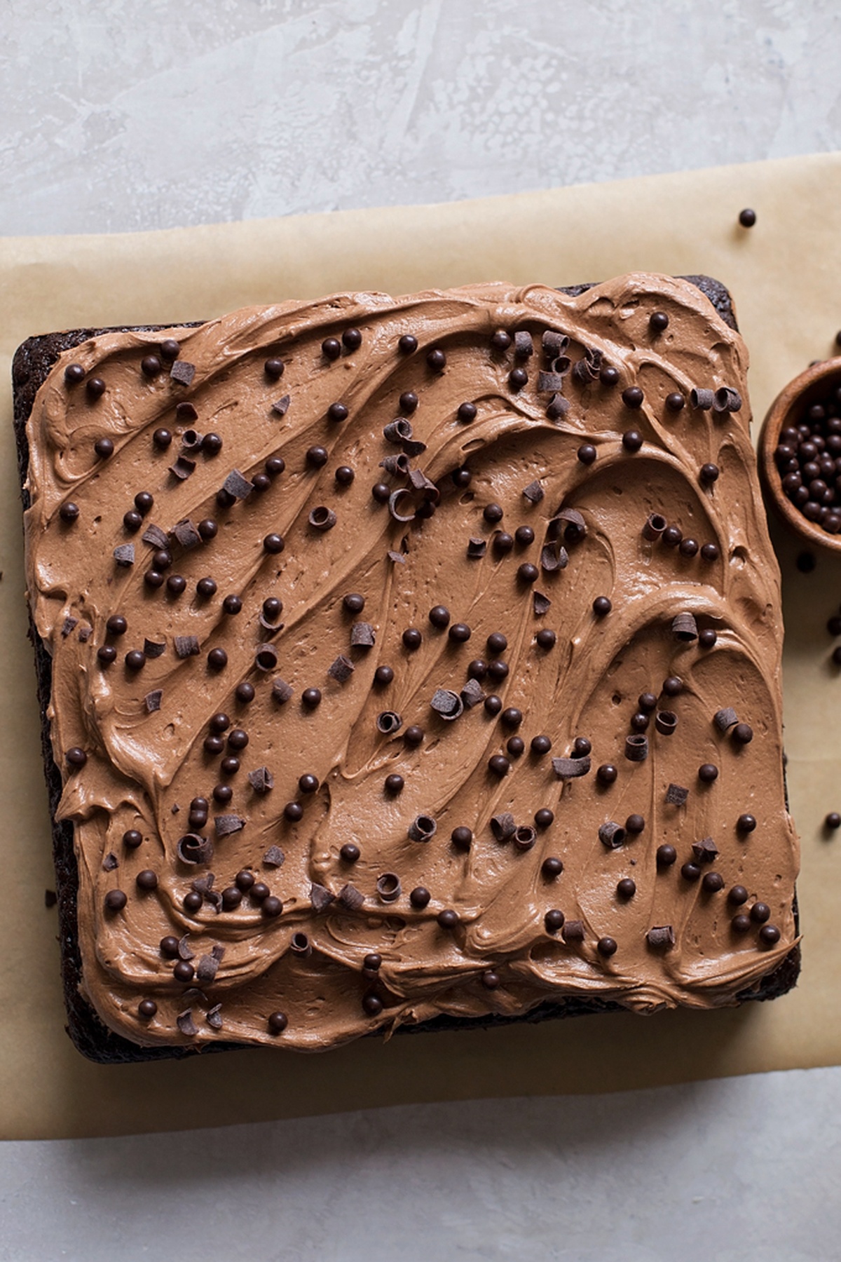 Square cake on parchment paper topped with chocolate curls.