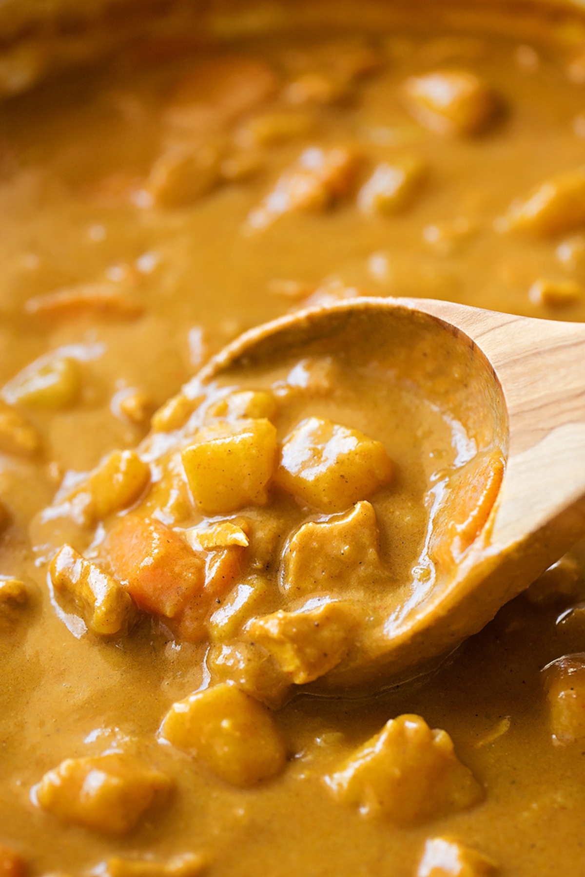 Creamy yellow coconut curry being served with a wooden spoon.