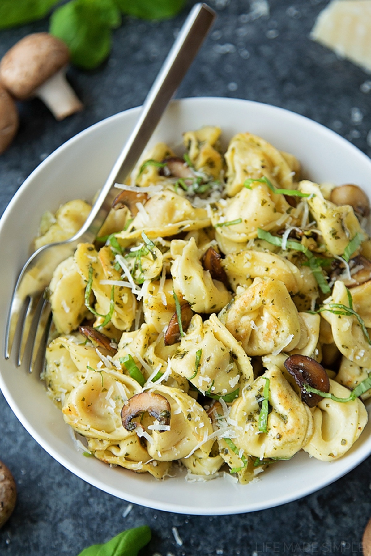 A bowl of tortellini with mushrooms and pesto.