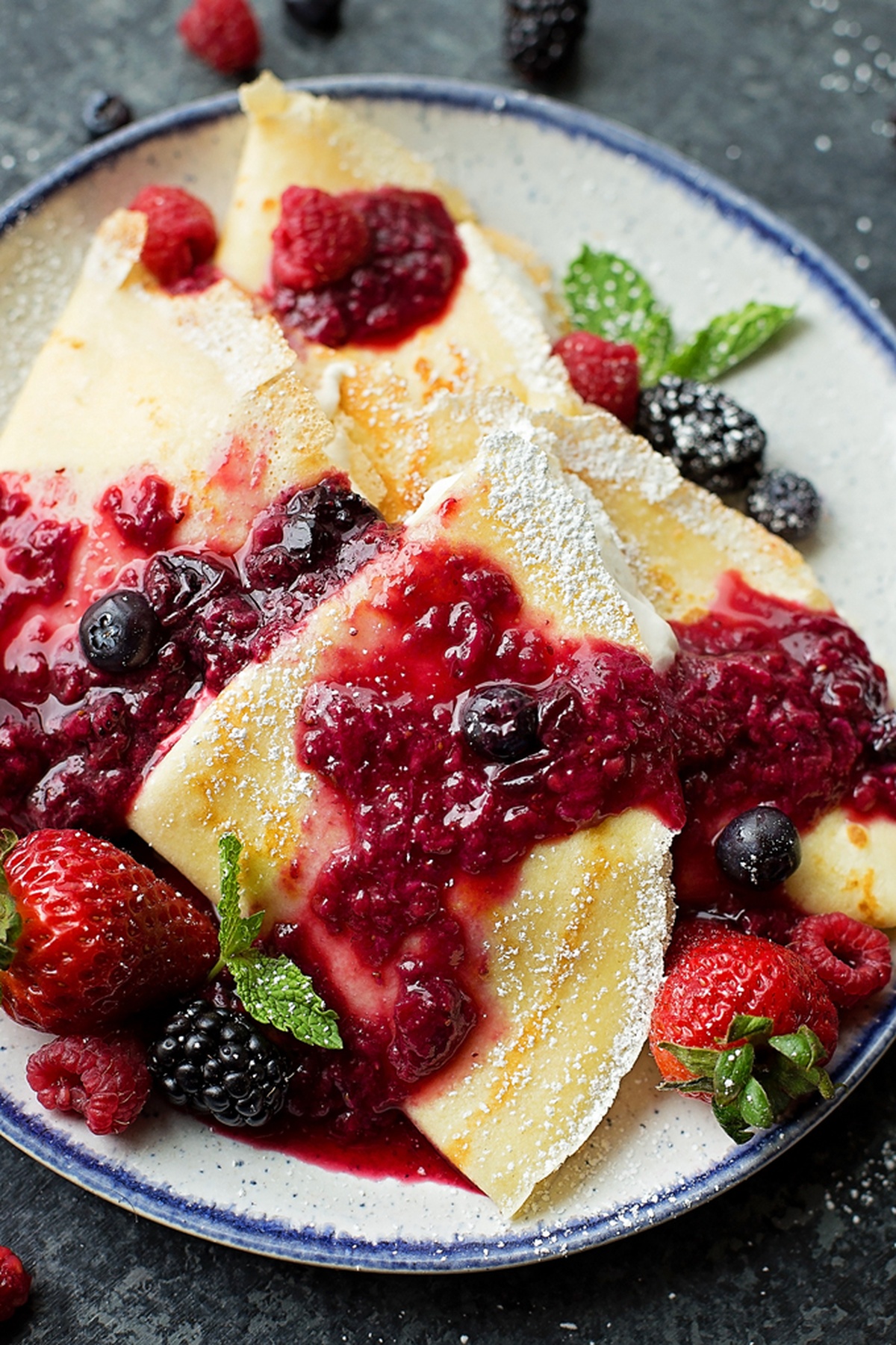Crepes topped with berry sauce and garnished with mint.