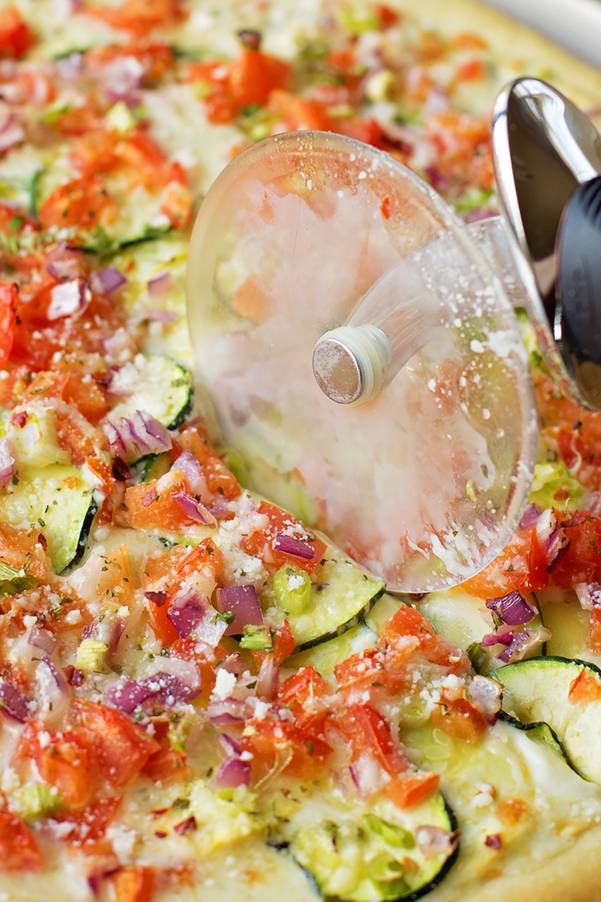 Pizza cutter slicing through a freshly baked vegetable pizza.