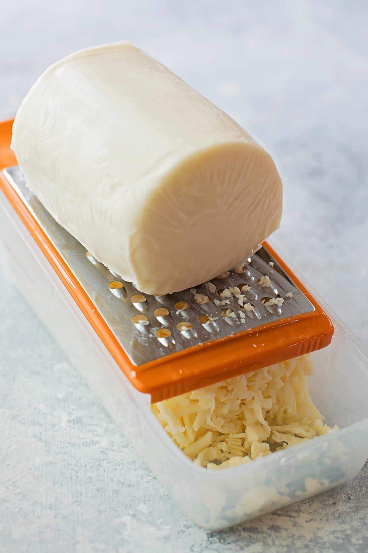 Block of cheese being grated with an orange-handled grater.