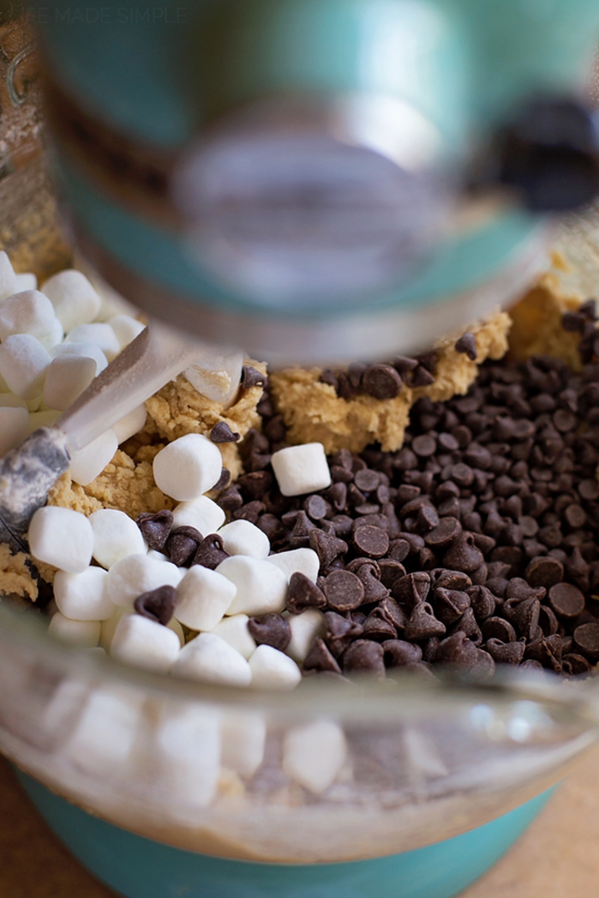 Mixing marshmallows and chocolate chips into cookie dough with a stand mixer.