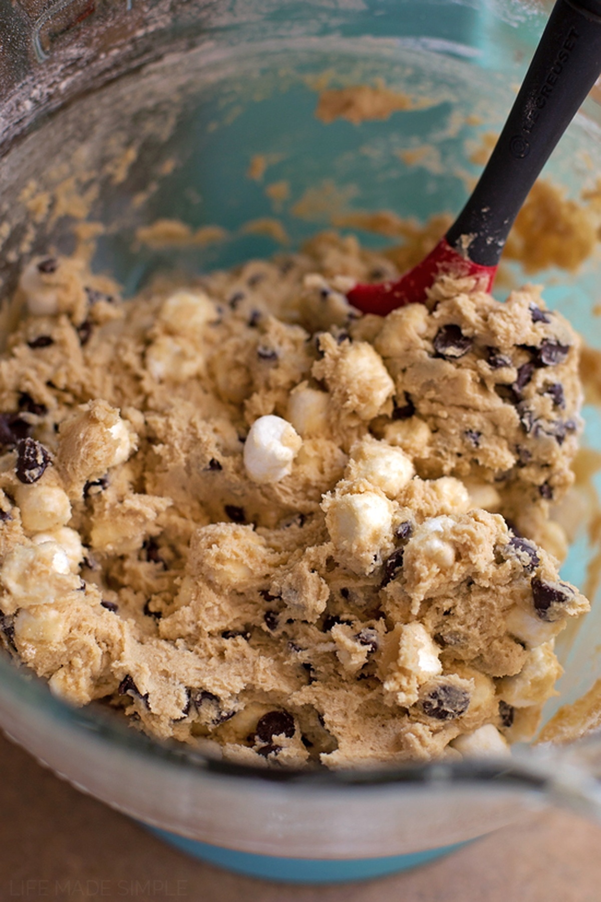 A bowl of cookie dough with marshmallows and chocolate chips being mixed with a spatula.