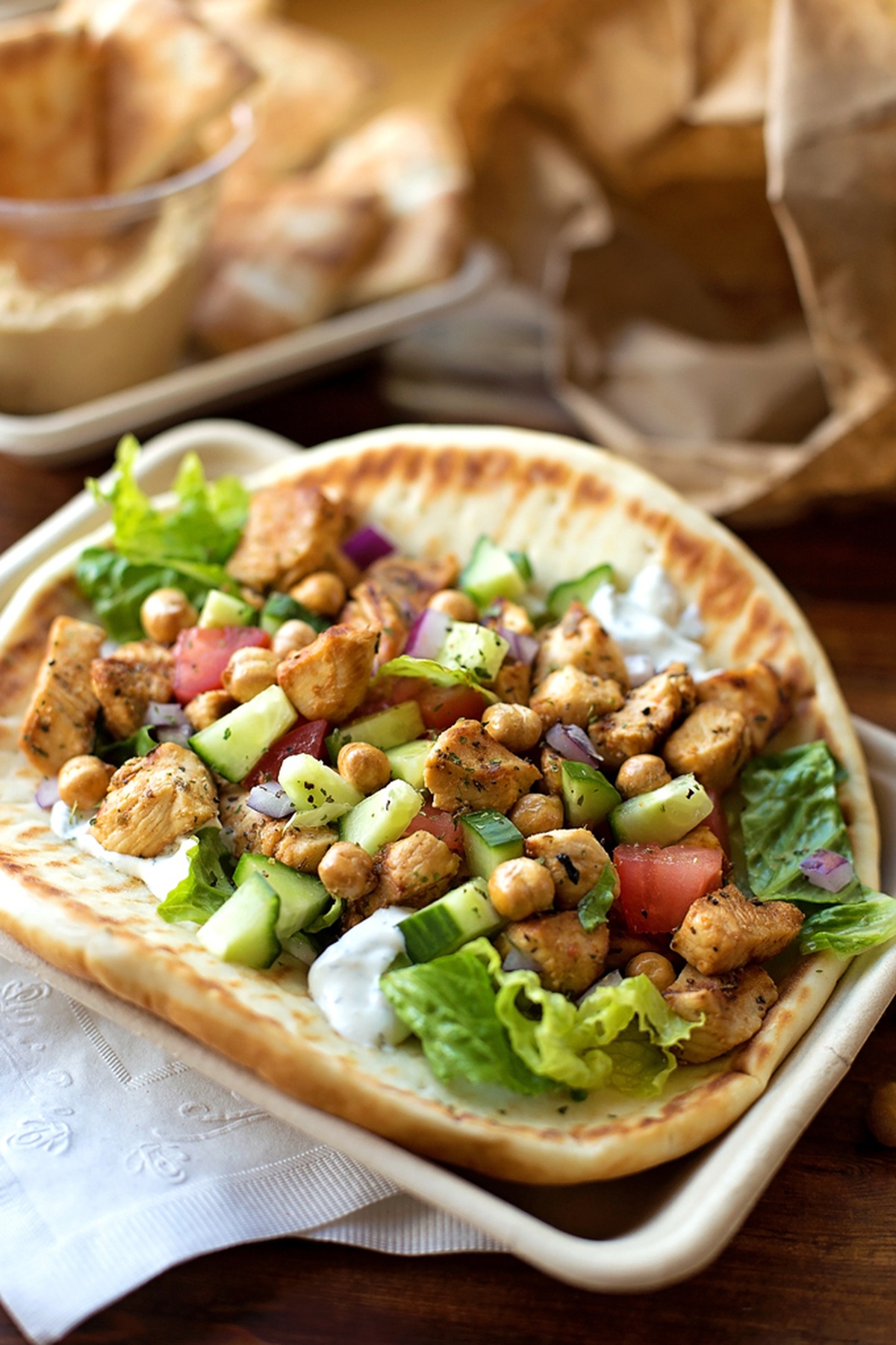 Open-faced grilled Greek chicken pita with fresh vegetables and chickpeas.
