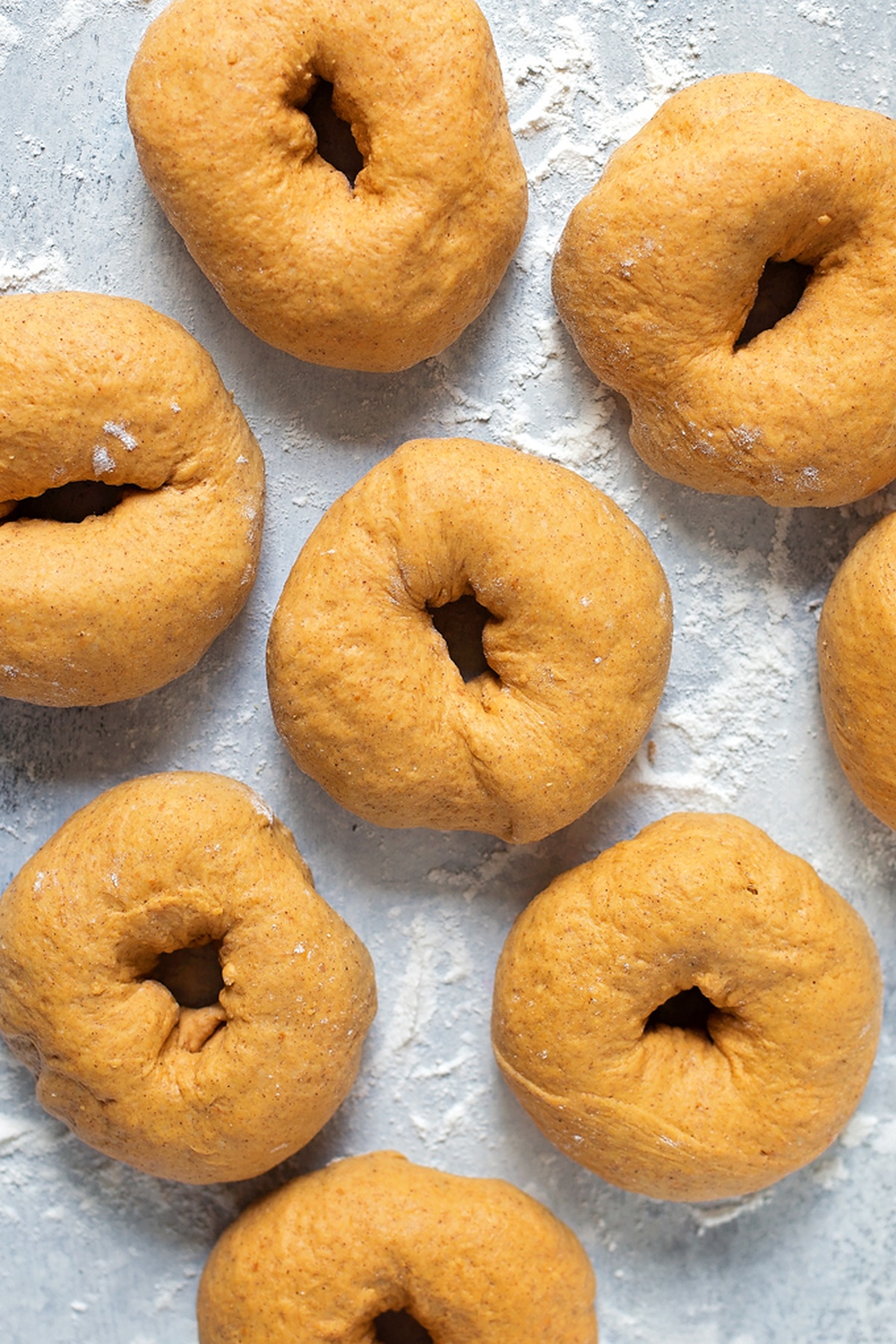 Shaped pumpkin bagels on a floured surface.