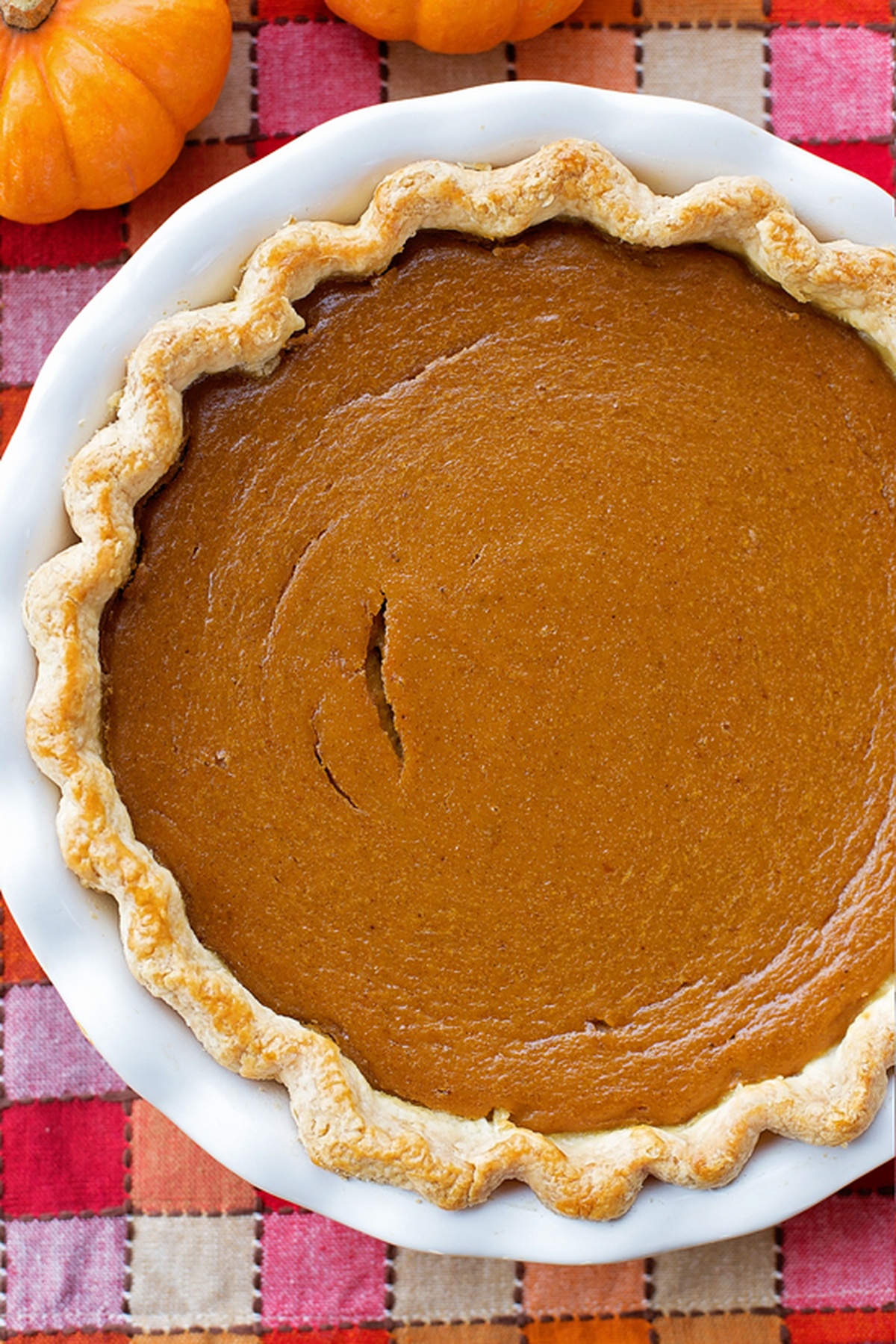 Whole pumpkin pie with a golden crust on a white dish.
