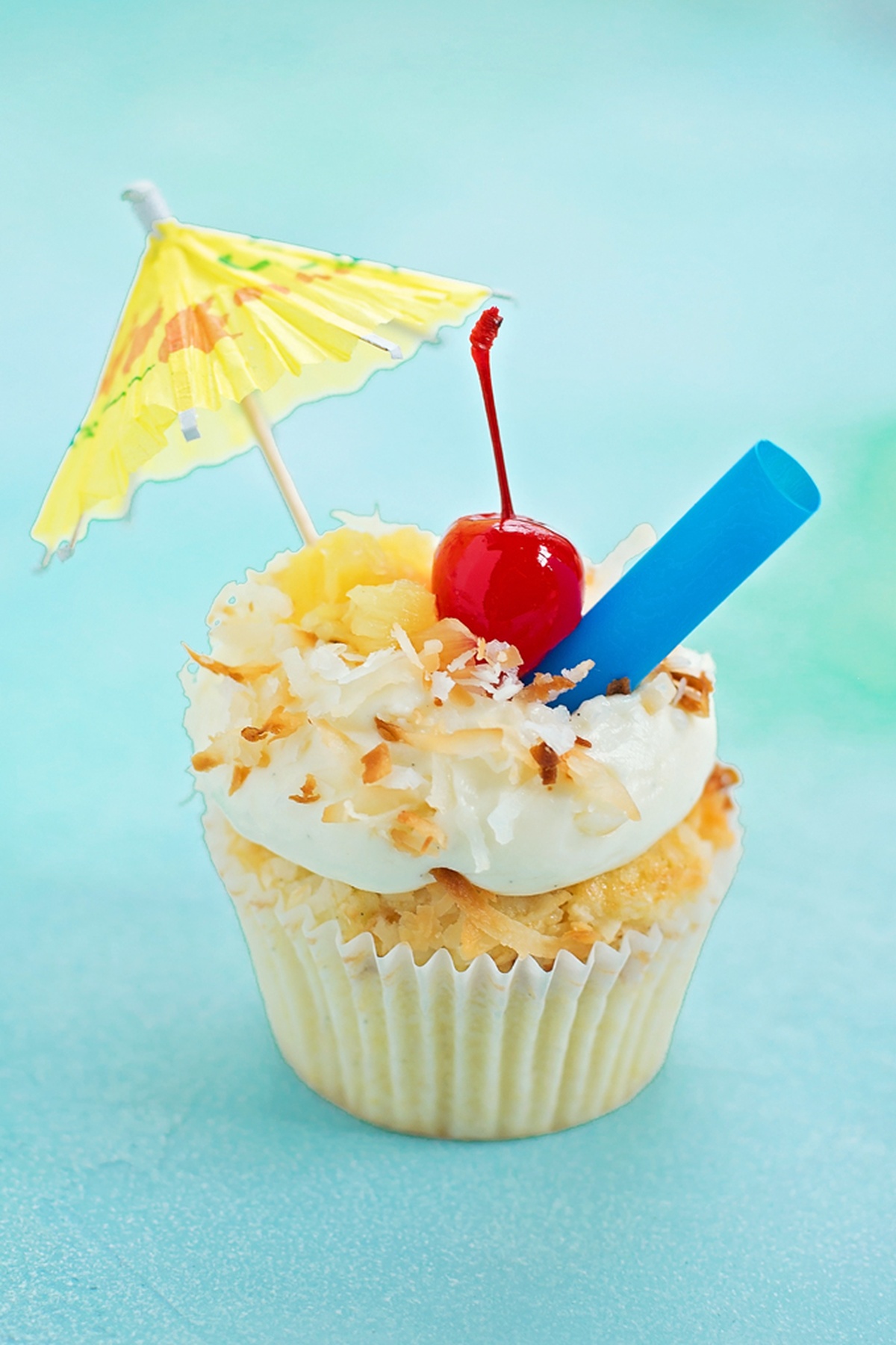 Pi&ntilde;a Colada Cupcake with a cherry, straw, and umbrella, decorated with coconut and cream.