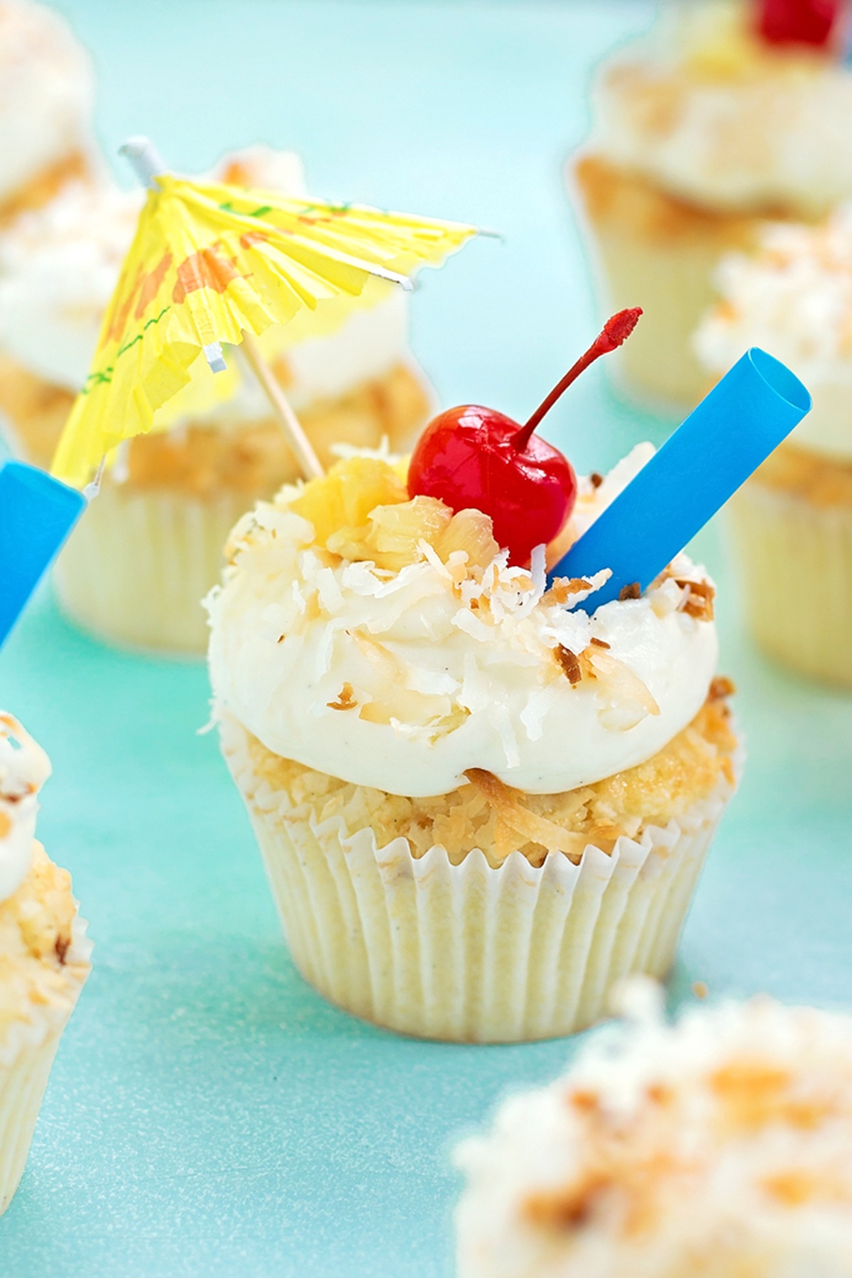 A tropical cupcake with a cherry and umbrella on a bright yellow background.