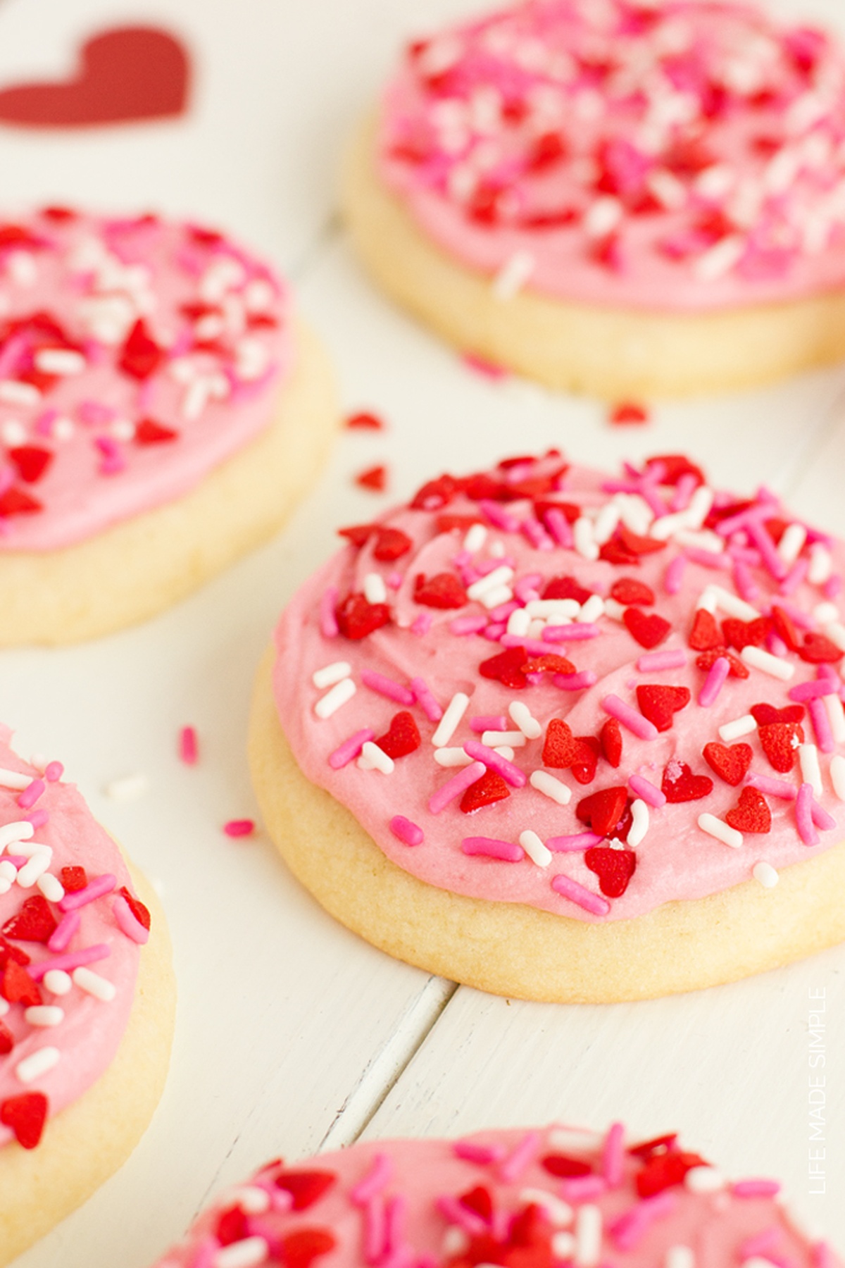 Giant thick Bakery Style Sugar Cookies taste just like Lofthouse cookies, only 10x better! They are melt-in-your-mouth delicious. Close-up of pink frosted sugar cookies with red and white sprinkles.