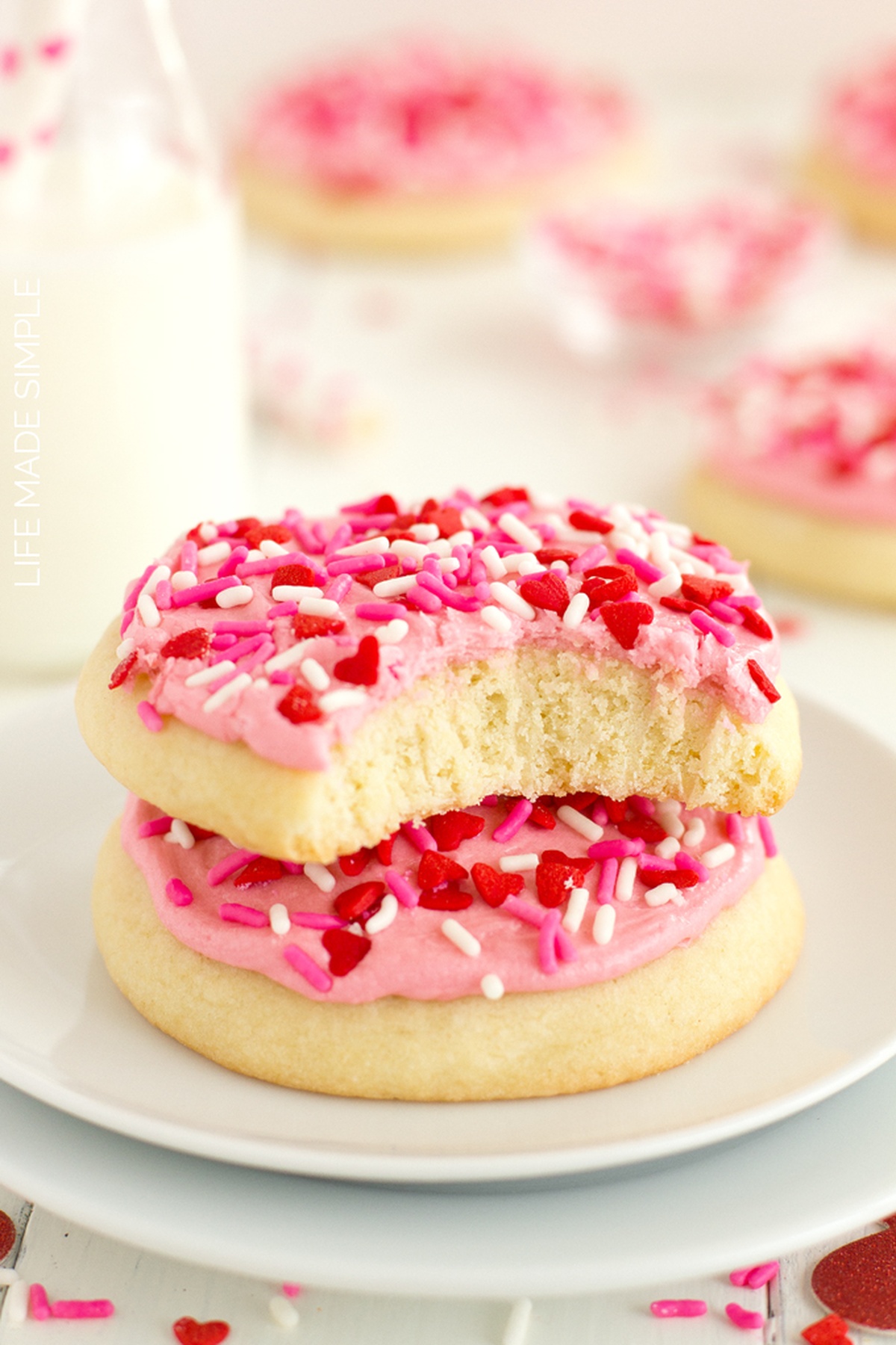 Two pink frosted sugar cookies stacked with a bite taken out of the top cookie.