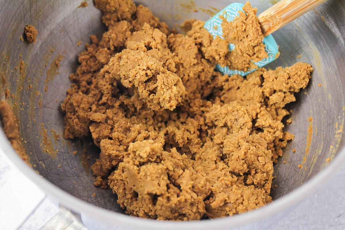 Thick ginger cookie dough in a large mixing bowl with a blue spatula.