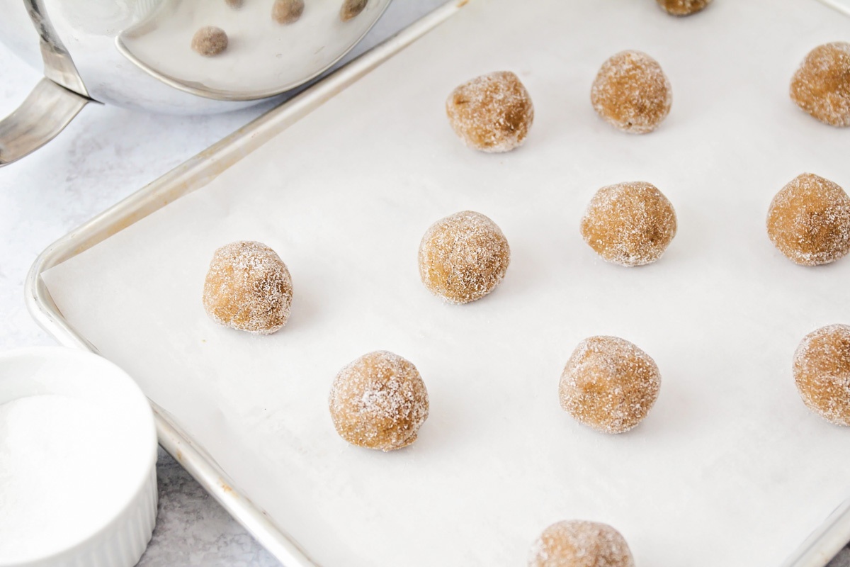 Balls of ginger cookie dough rolled in sugar and placed on a parchment-lined baking sheet.