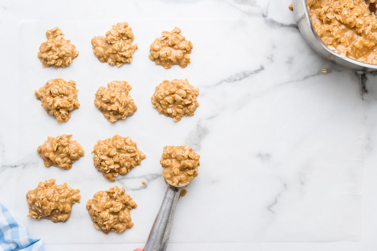 Scooping no-bake peanut butter cookie mixture onto a sheet.