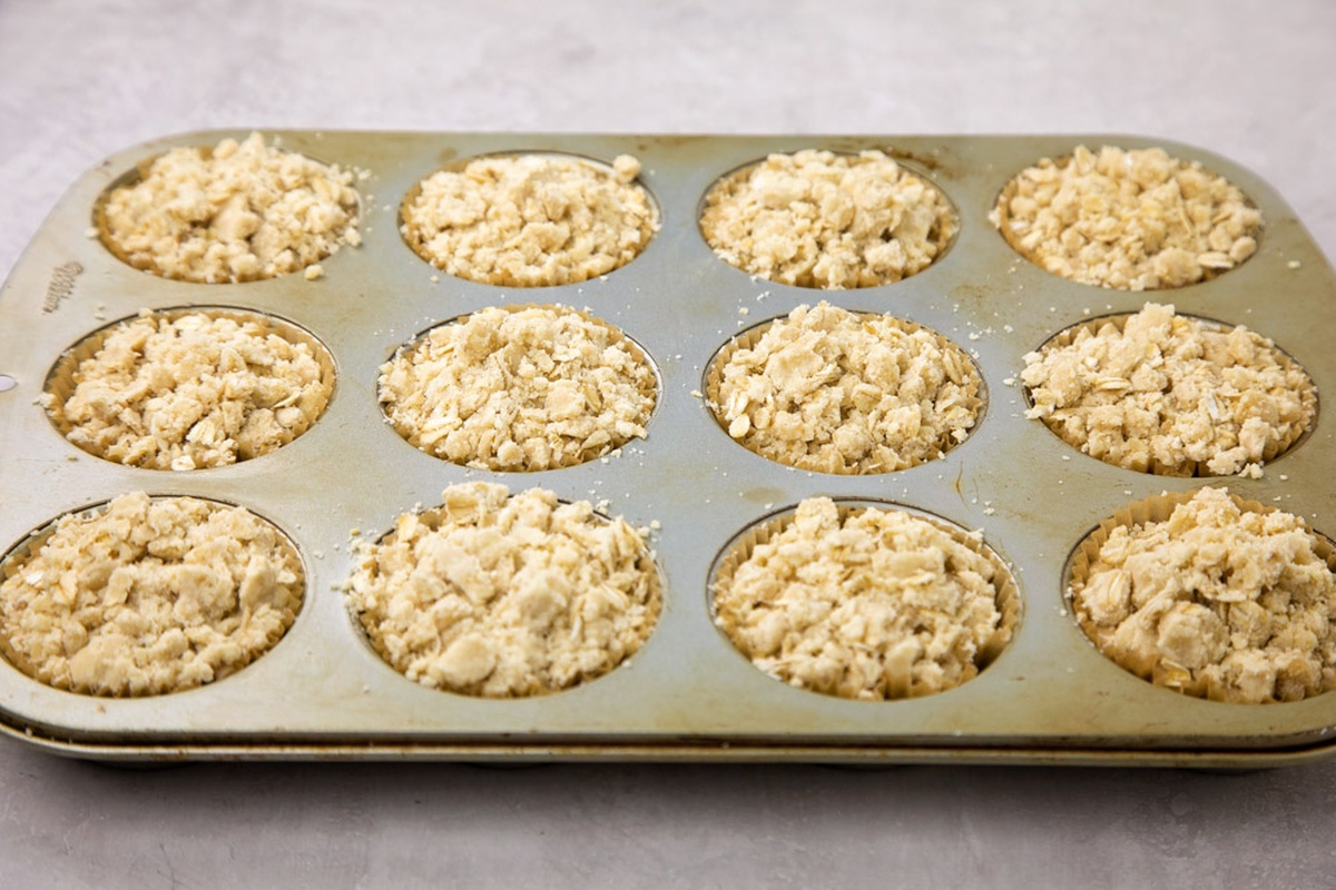 Muffin tin filled with oatmeal crumb muffin batter and topping.