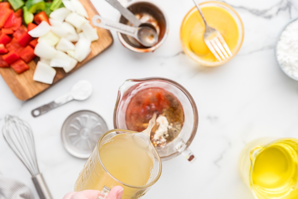 Pouring chicken stock into the sauce mixture.
