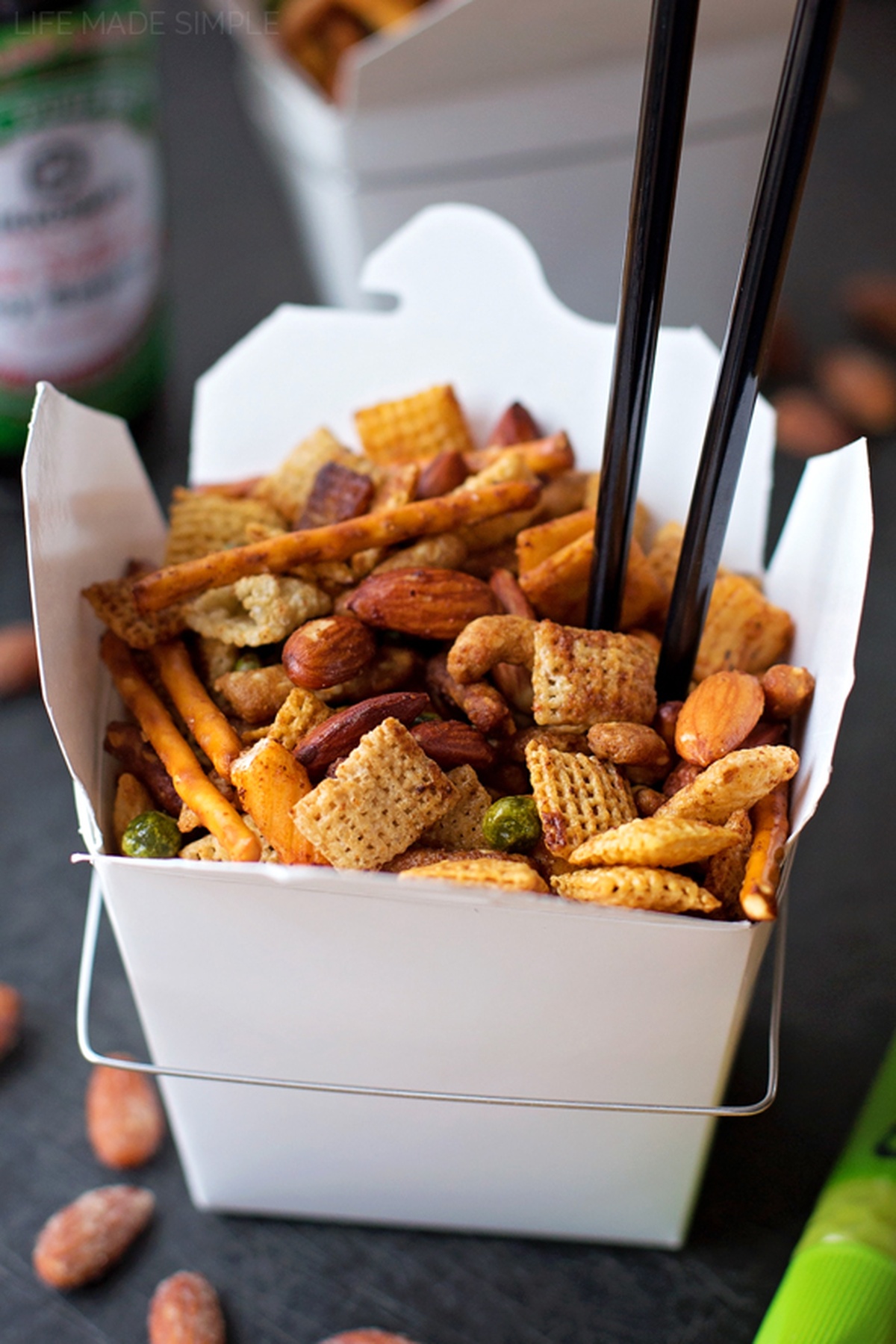 A white takeout box of Asian snack mix with chopsticks.
