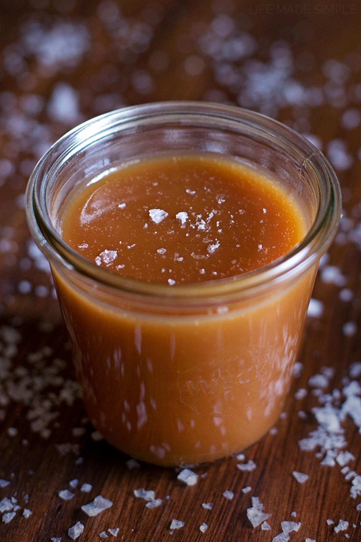 A jar of caramel sauce sprinkled with sea salt on a wooden surface.