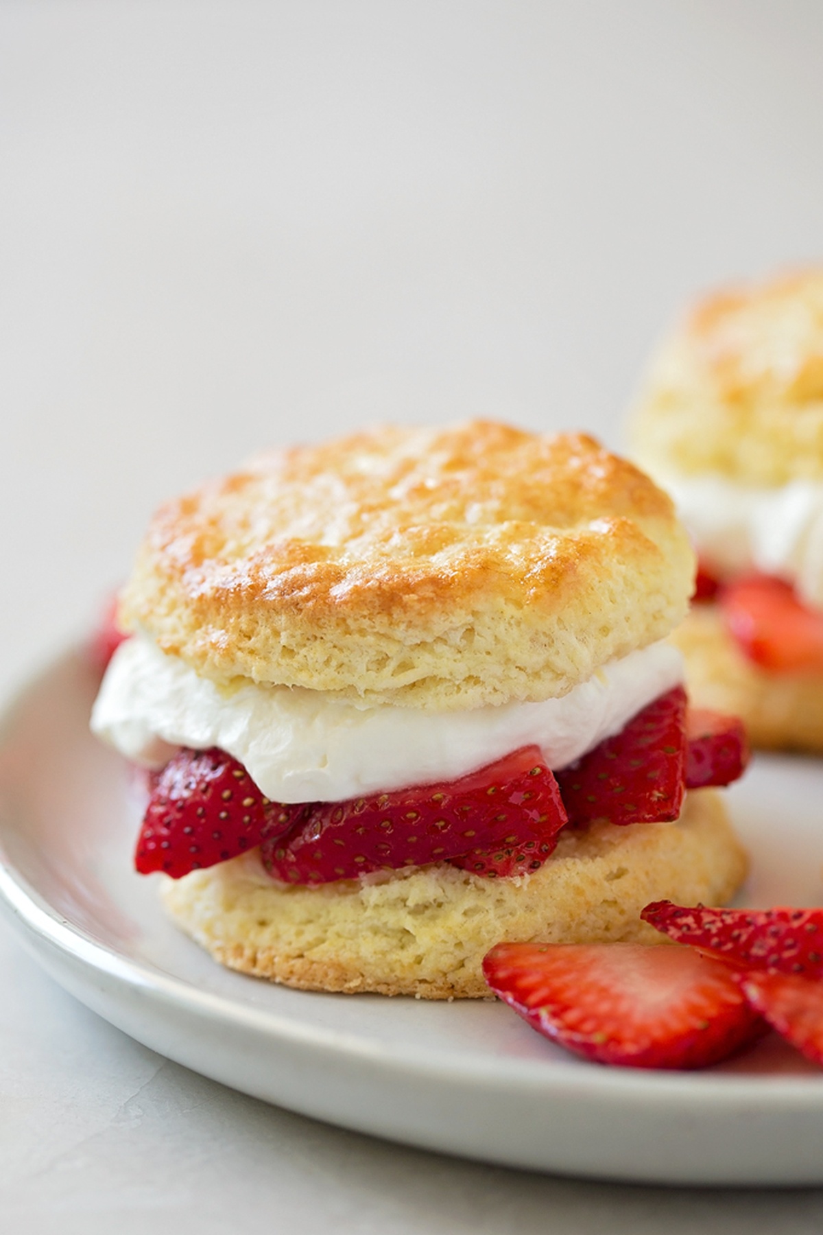 Strawberry shortcakes topped with whipped cream and sliced strawberries on a white plate.
