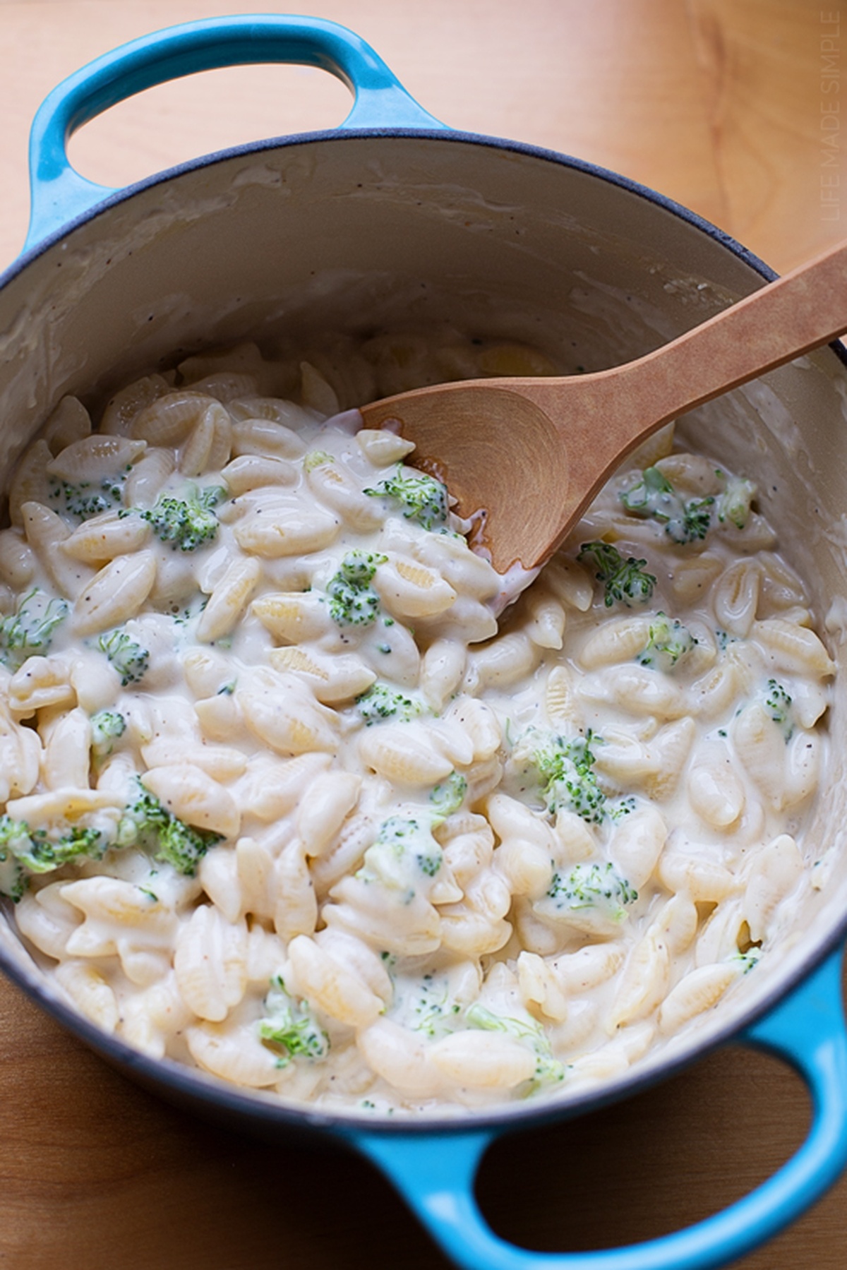 White cheddar pasta being stirred in a blue pot with a wooden spoon.