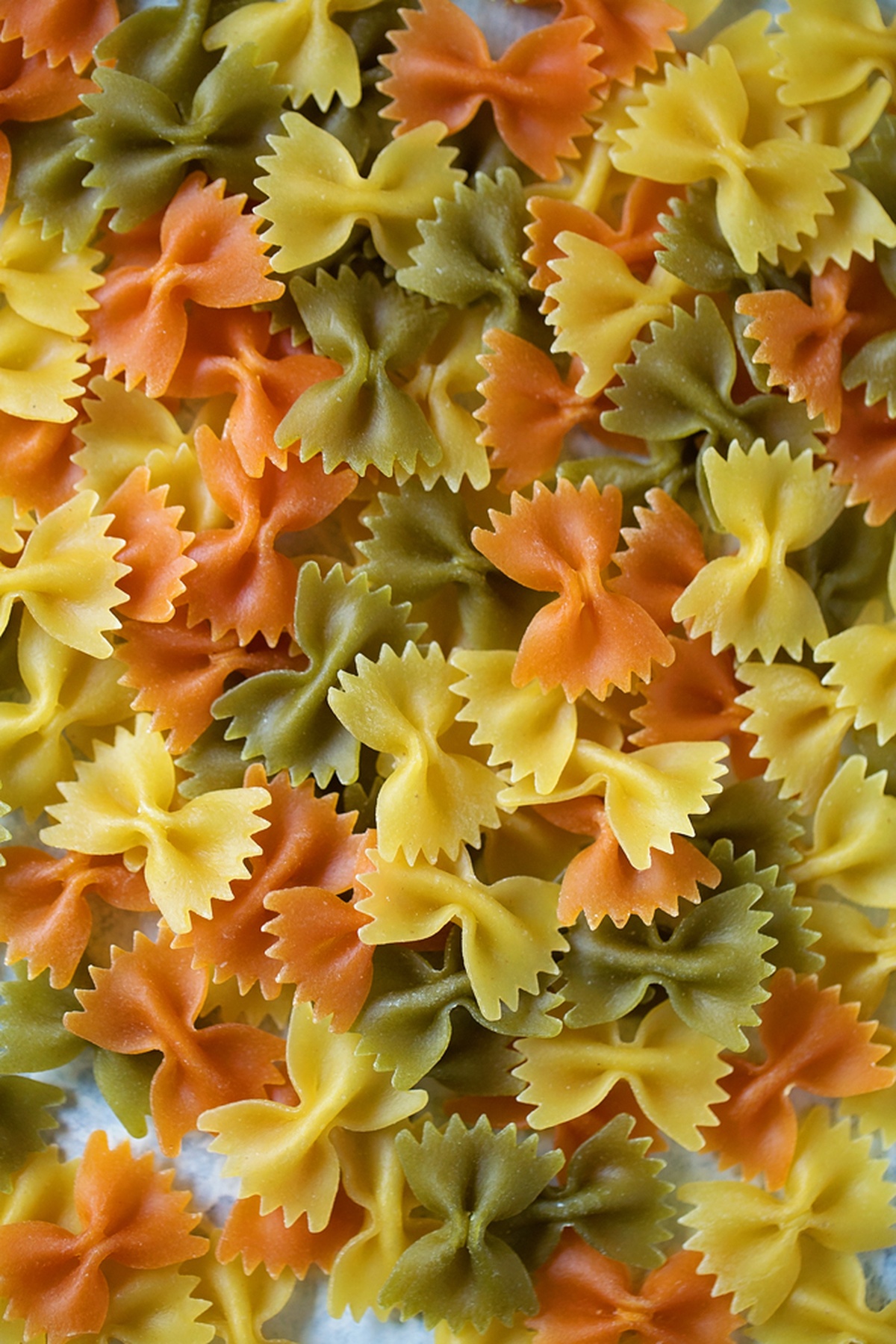 Tri-colored uncooked bowtie pasta spread out for zesty Italian pasta salad recipe.