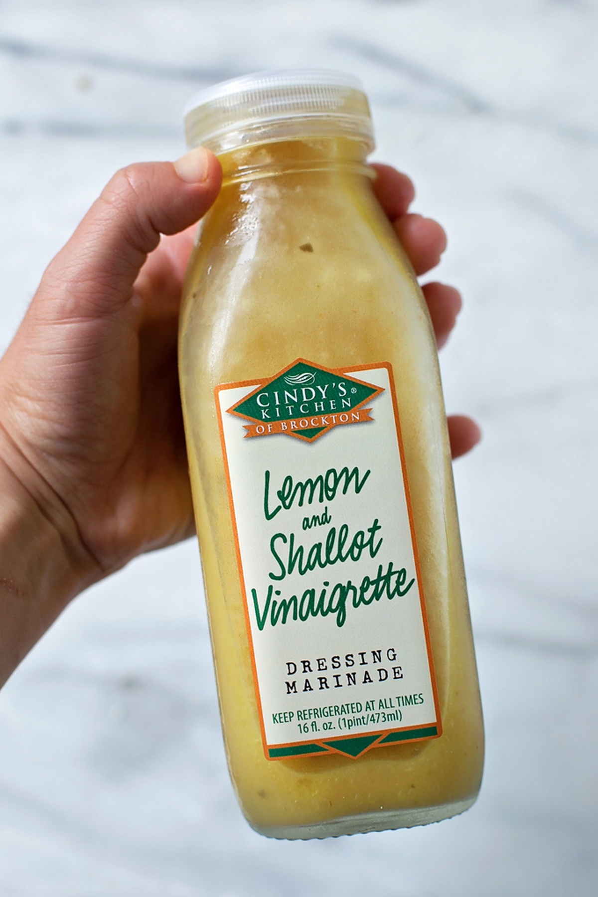 Hand holding a bottle of lemon and shallot vinaigrette.