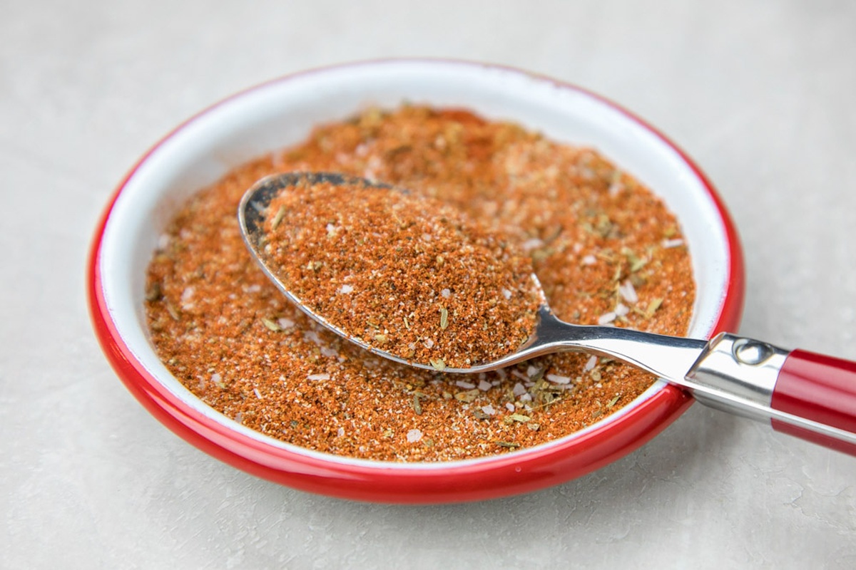 A spoon filled with taco seasoning resting on a bowl of seasoning.