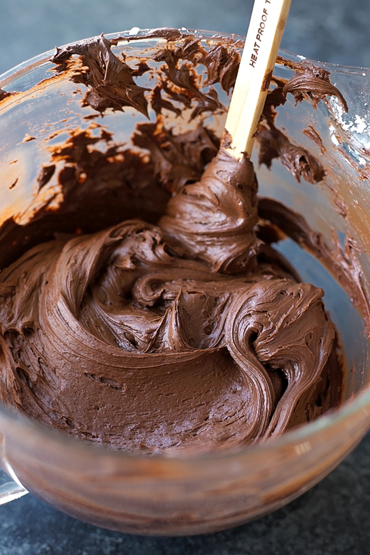 A bowl of smooth chocolate frosting being mixed with a spatula.
