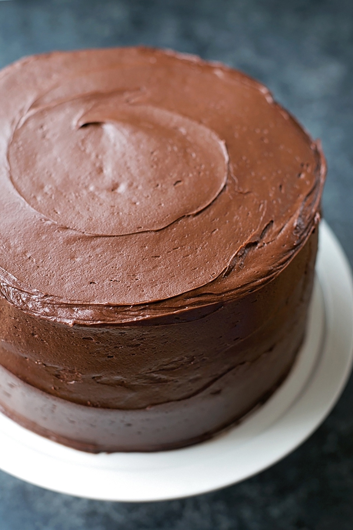 Fully frosted, smooth chocolate blackout cake on a white cake stand.