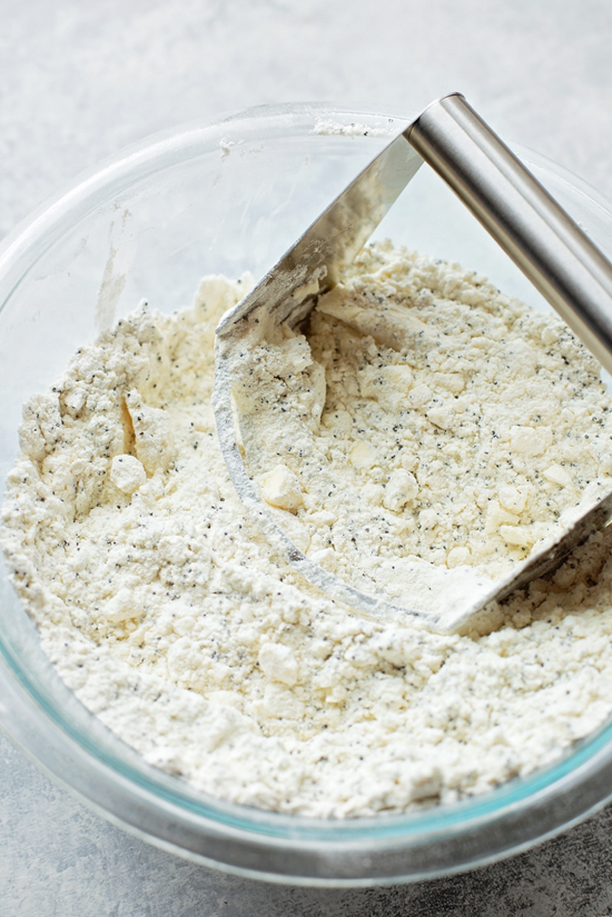 A mixing bowl with scone ingredients, being combined with a pastry cutter.