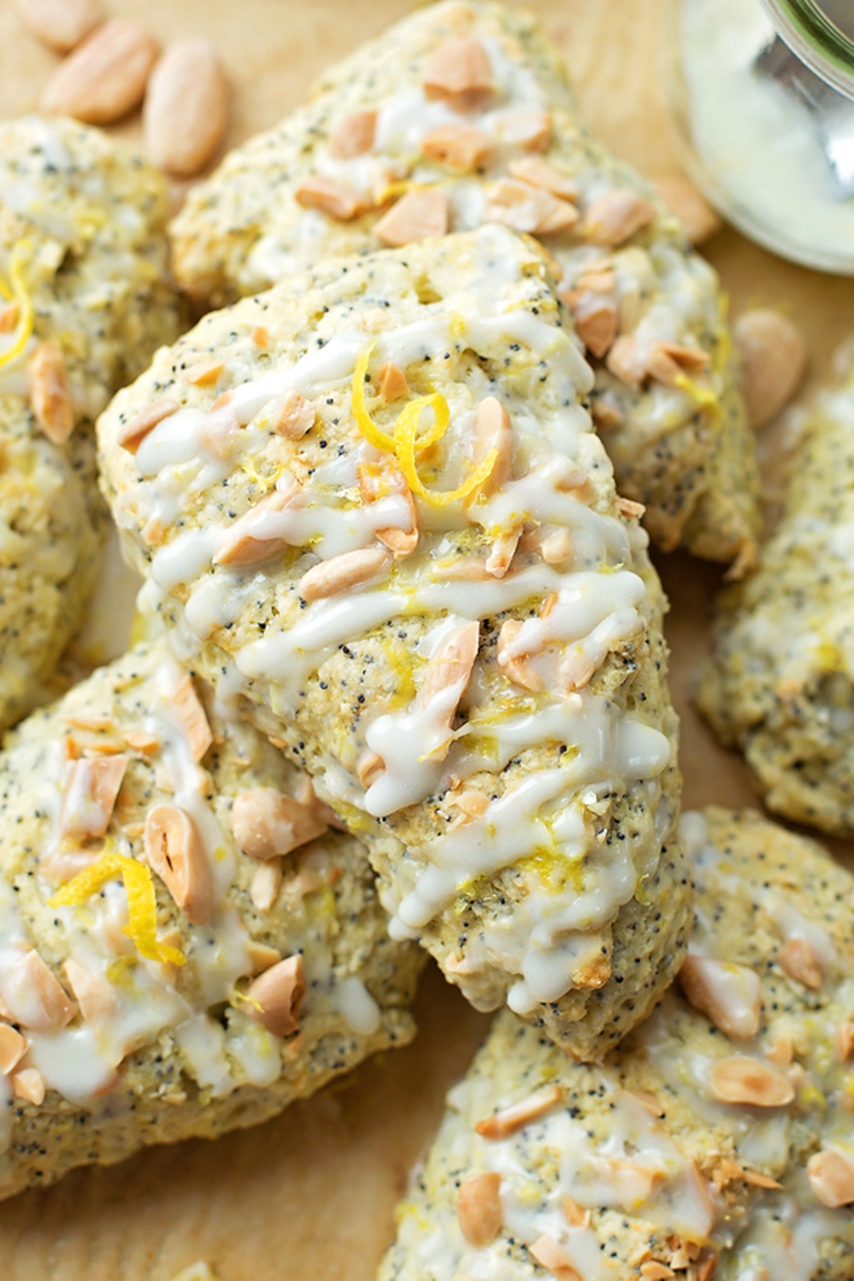 Overhead view of lemon scones with a lemon glaze, garnished with slivered almonds and lemon zest on a baking sheet.