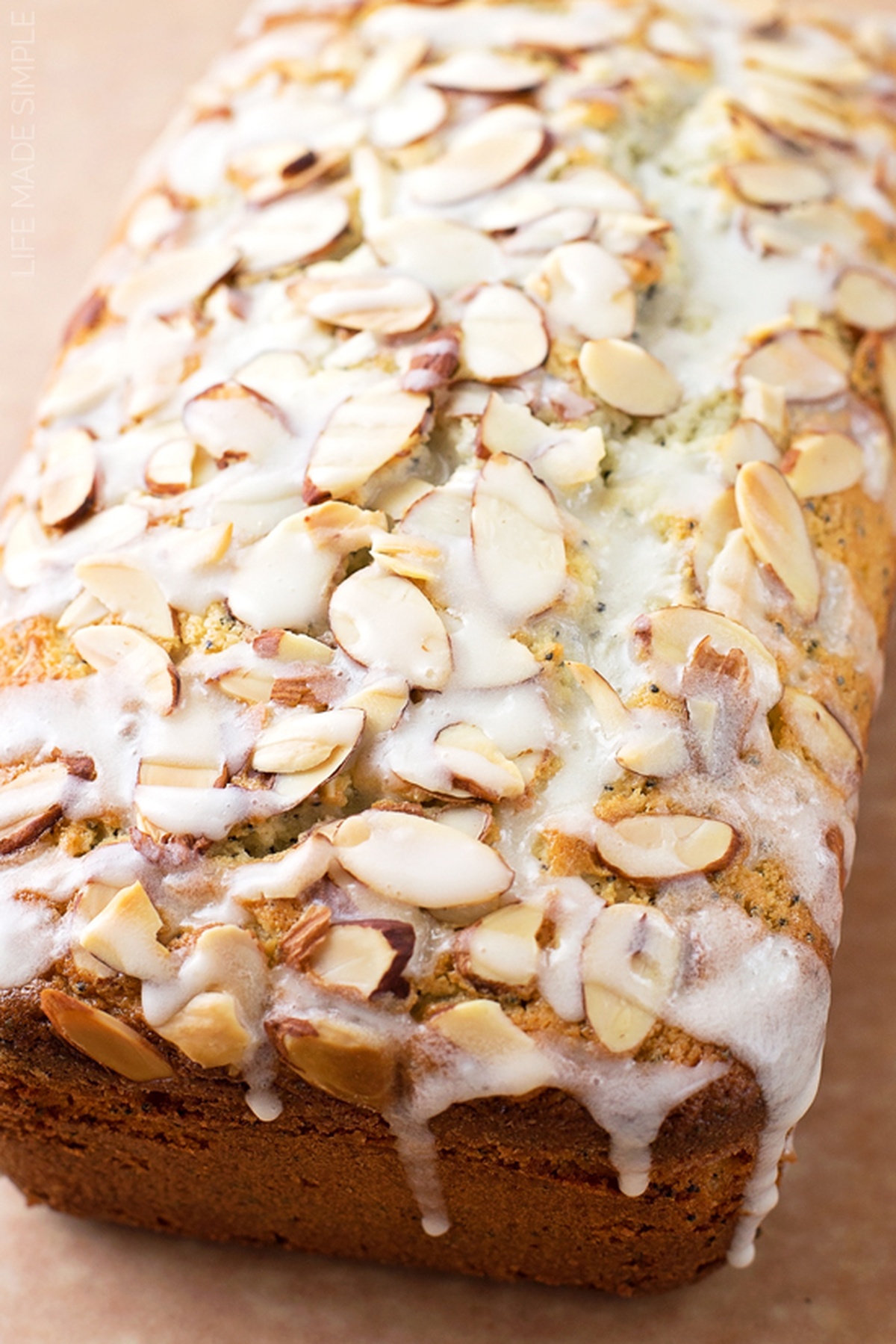 Close-up of a loaf of poppy seed almond bread with a drizzle of icing and almond slices on top.